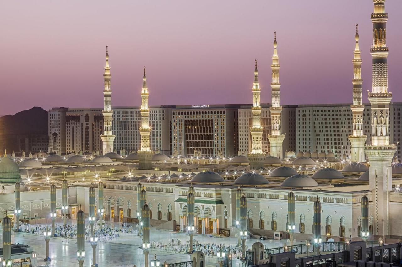 Готель Intercontinental Dar Al Iman Madinah By Ihg Medina Екстер'єр фото The photo shows a view of an expansive mosque complex, featuring several tall minarets that are illuminated against a twilight sky. The structure appears grand and is likely adorned with intricate architectural details. There are people gathered in t