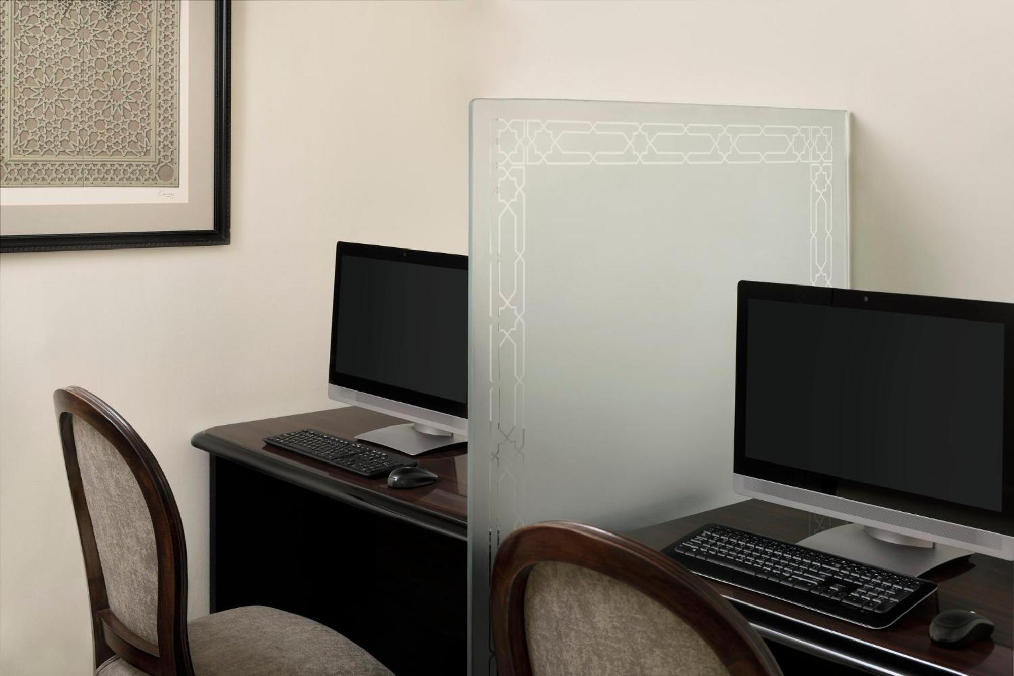 Готель Intercontinental Dar Al Iman Madinah By Ihg Medina Екстер'єр фото The photo shows a small office or workspace area featuring two computer stations. Each station has a black monitor, a keyboard, and appears to be set up on a dark wooden desk. A translucent glass partition is placed between the two workstations, prov