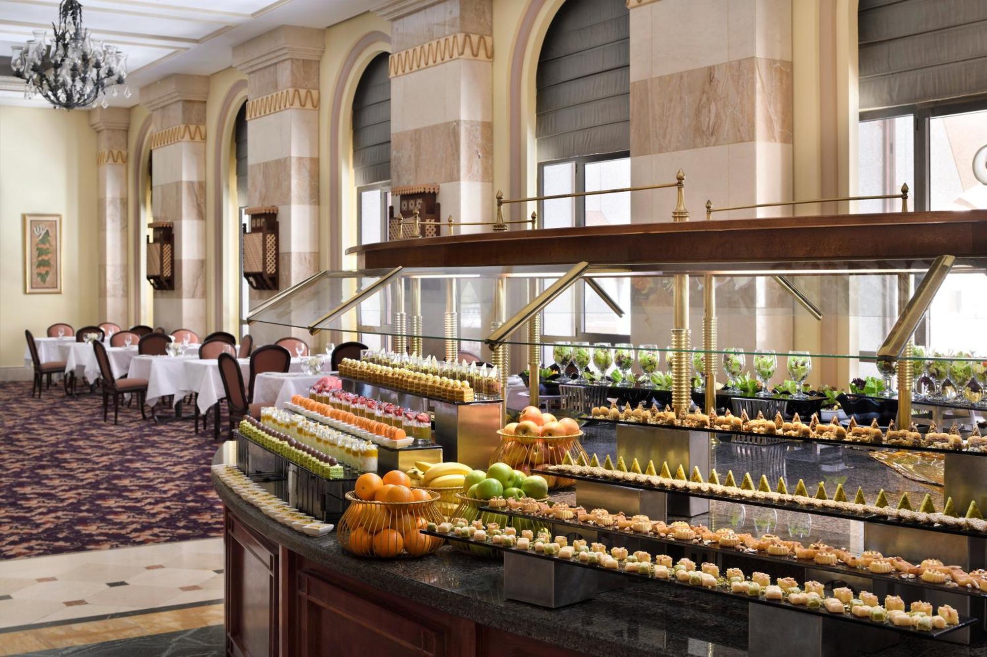 Готель Intercontinental Dar Al Iman Madinah By Ihg Medina Екстер'єр фото The photo depicts an elegant dining area featuring a buffet-style display. In the foreground, a beautifully arranged buffet counter showcases an array of desserts, including miniature pastries and colorful fruit. The setting has a sophisticated ambia