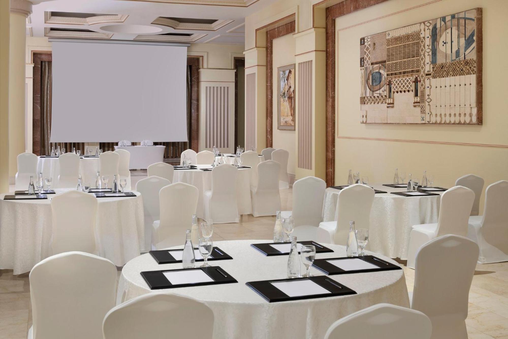 Готель Intercontinental Dar Al Iman Madinah By Ihg Medina Екстер'єр фото The photo shows a well-decorated event space or meeting room. It features several round tables covered with white tablecloths and surrounded by white chairs. Each table has black placemats and glass water bottles, suggesting a formal setup for a gath