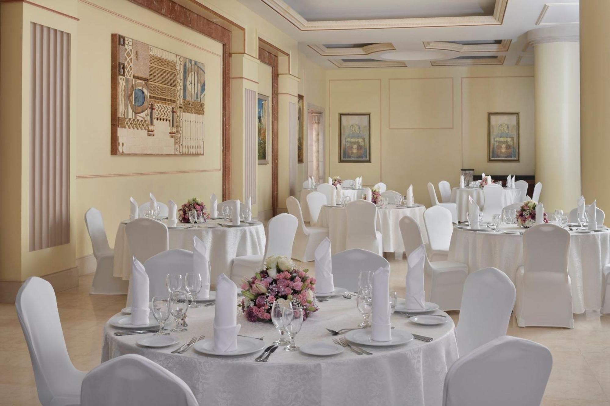 Готель Intercontinental Dar Al Iman Madinah By Ihg Medina Екстер'єр фото The photo shows an elegantly arranged dining or function room. There are round tables covered with white tablecloths, each set with fine dining ware including glassware, utensils, and neatly folded white napkins. Some tables have floral centerpieces 