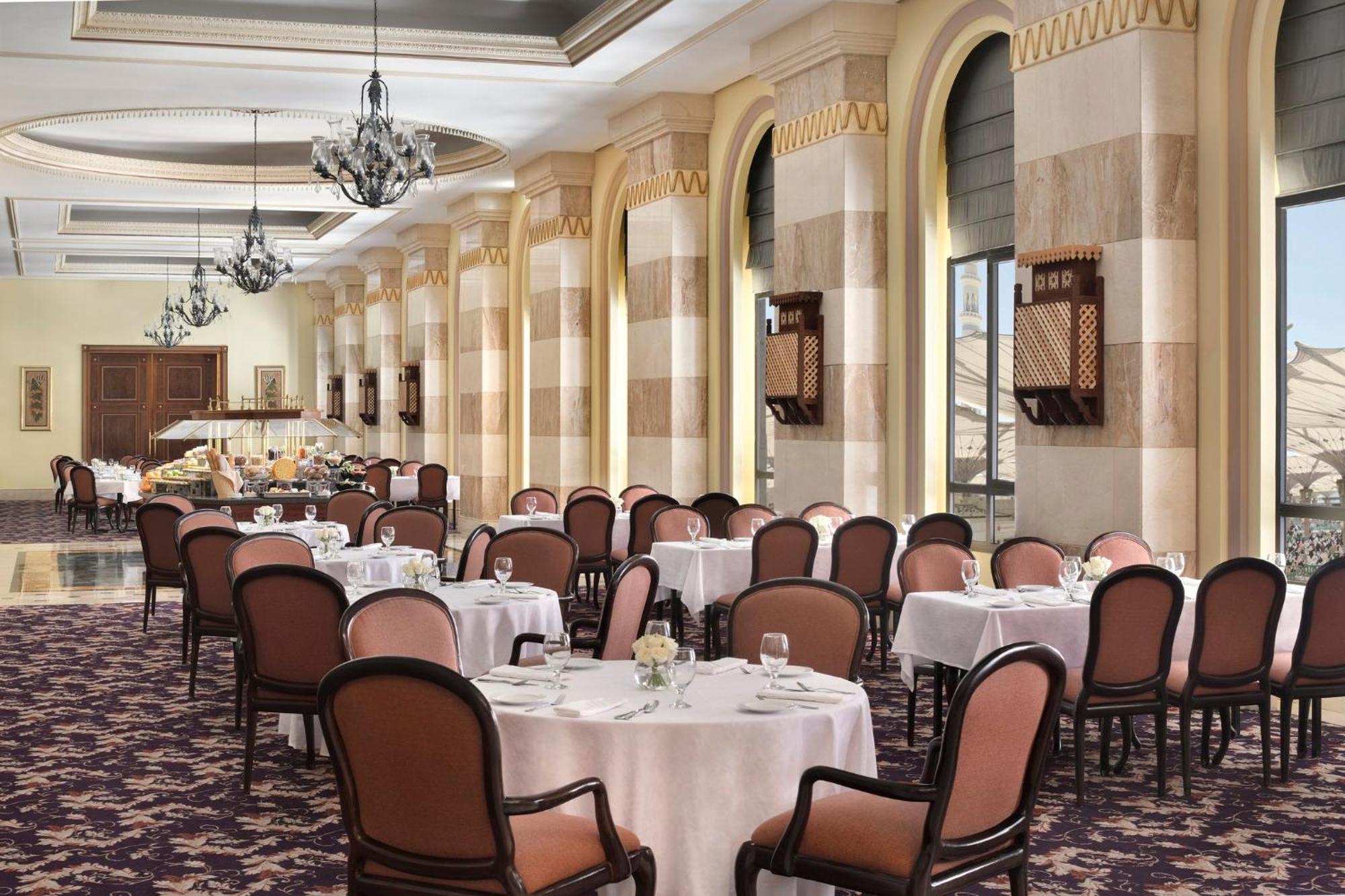 Готель Intercontinental Dar Al Iman Madinah By Ihg Medina Екстер'єр фото The photo depicts an elegant dining room setting. It features several round tables covered with white tablecloths, each set with dishes and glassware. The room has a sophisticated ambiance, characterized by high ceilings adorned with chandeliers and 