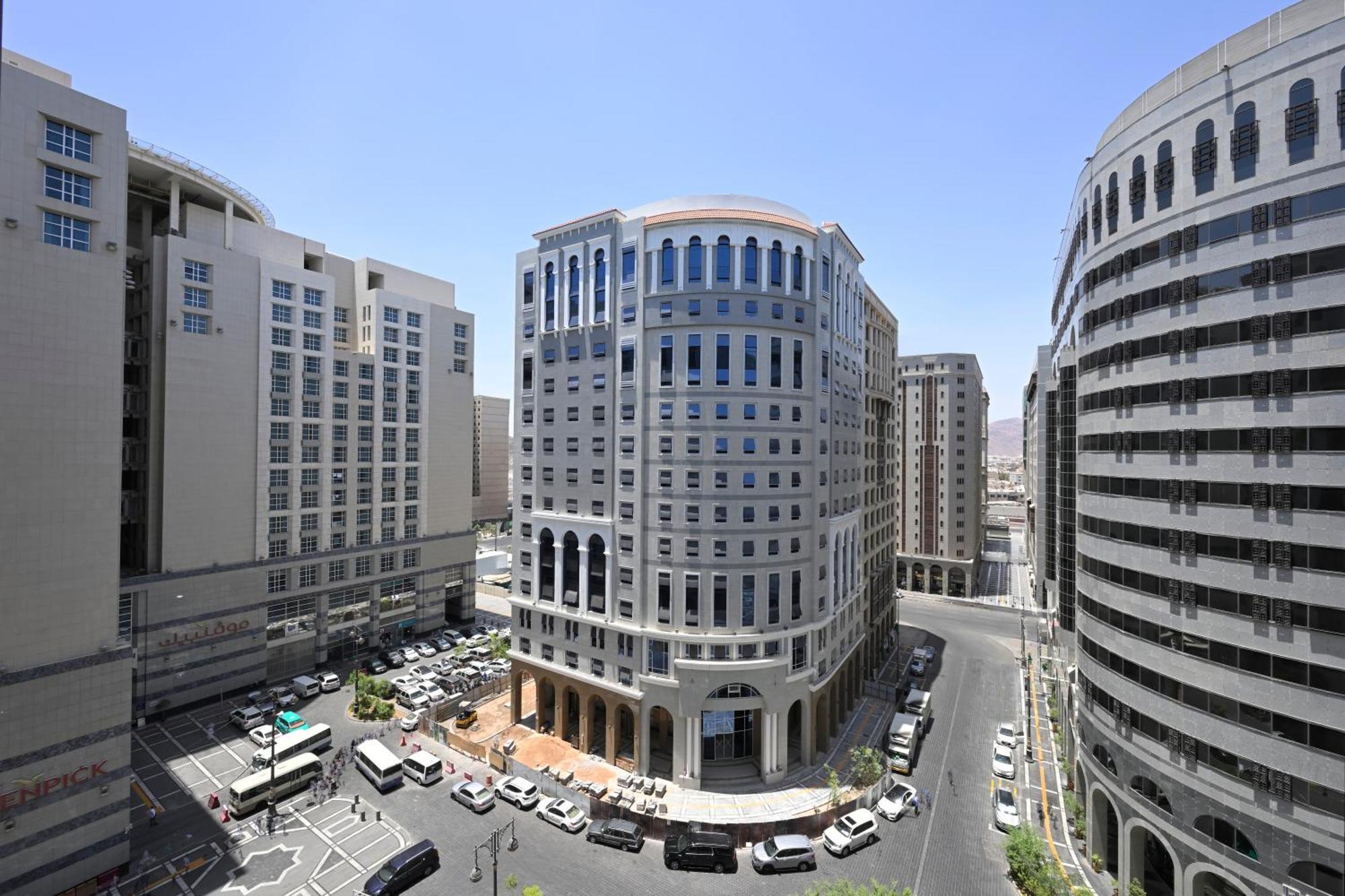 Готель Intercontinental Dar Al Iman Madinah By Ihg Medina Екстер'єр фото The photo shows a modern urban scene featuring several buildings, including a prominent rounded building with a glass façade. This building appears to be situated at an intersection, surrounded by other high-rise structures that have distinct archite