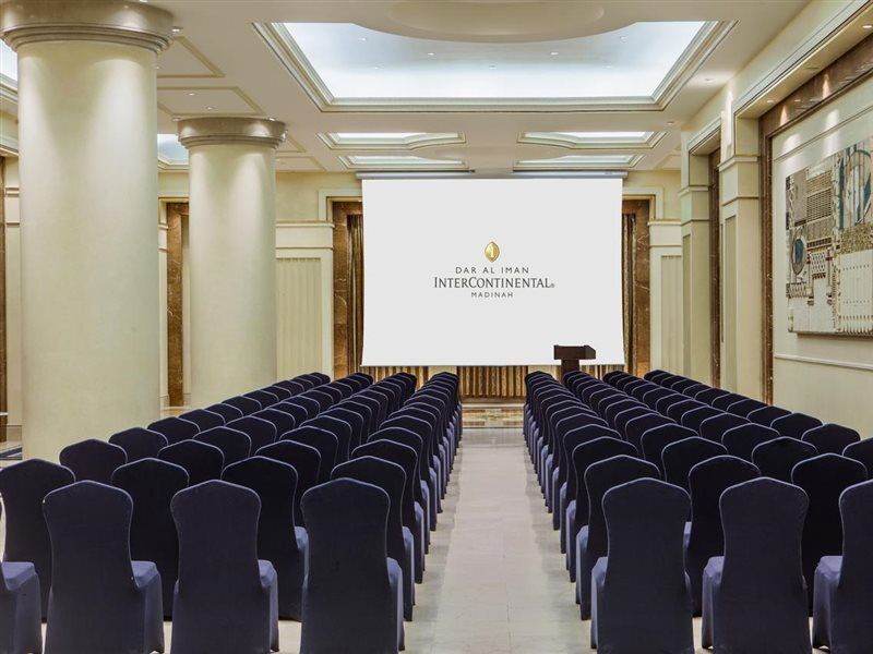 Готель Intercontinental Dar Al Iman Madinah By Ihg Medina Екстер'єр фото The photo shows a conference or meeting room set up. There are rows of dark blue chairs arranged facing a large screen at the front of the room. The screen displays the logo of the Intercontinental hotel, indicating that this space is likely intended